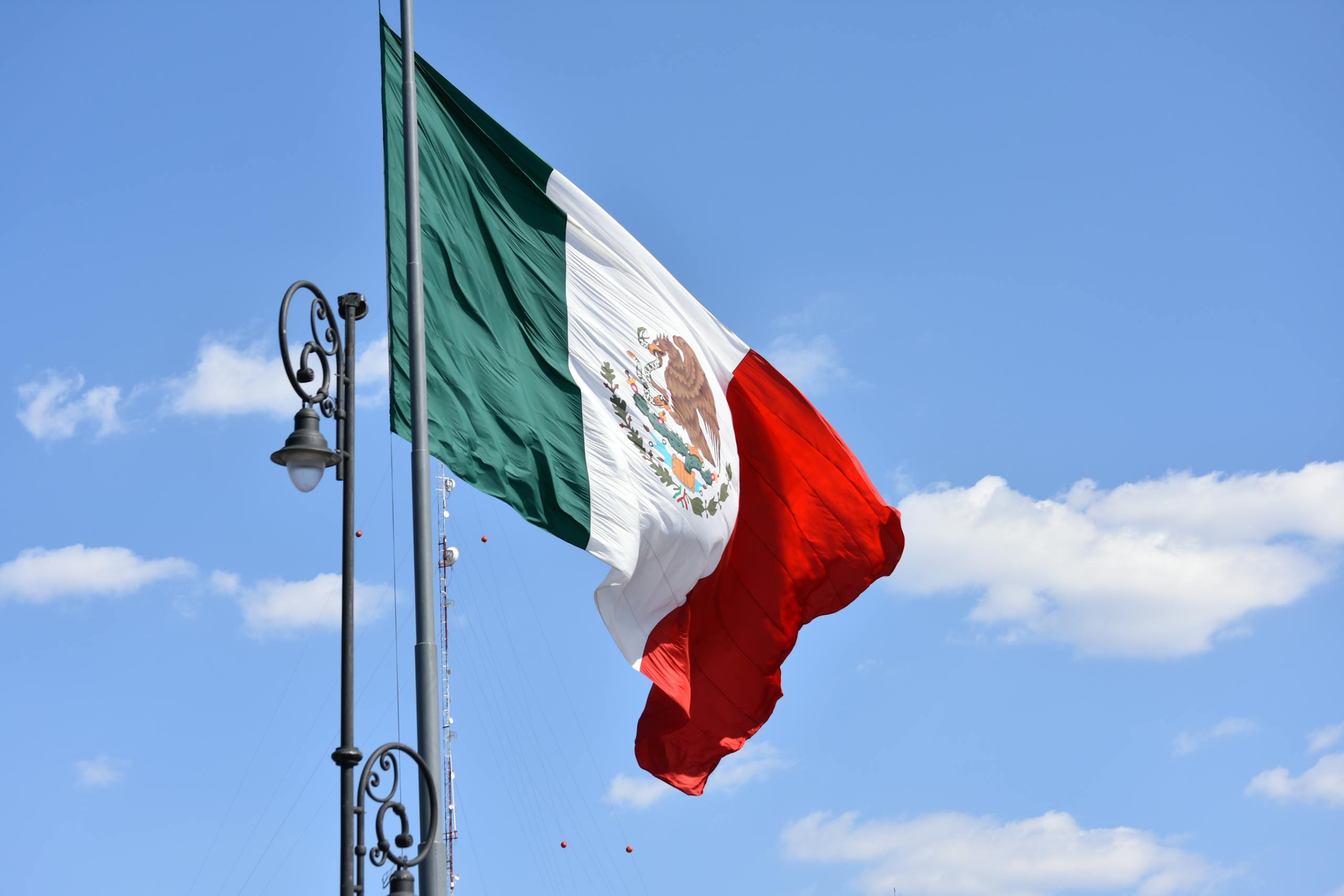 The Mexican flag swaying on a flagpole against a bright blue sky in Mexico City.